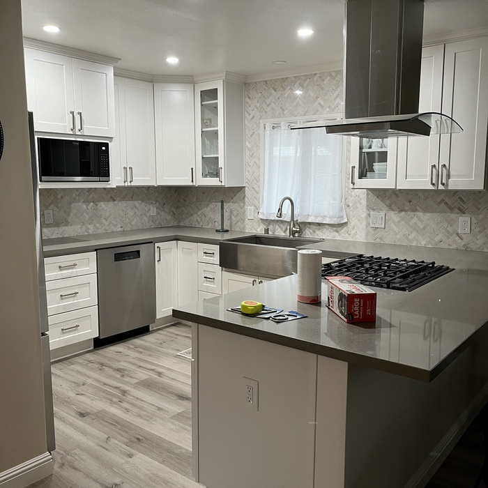 White shaker kitchen remodel with gray quartz island, gas range and herringbone backsplash by MG Construction